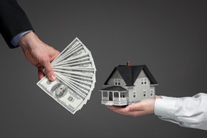 Close up of hands giving house model to other hands with money