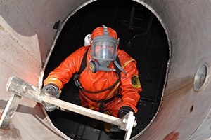 Man in chemical suit entering inside cargo tank on chemical ship