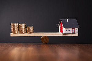 Seesaw with a house on one side and stacks of coins on the other side